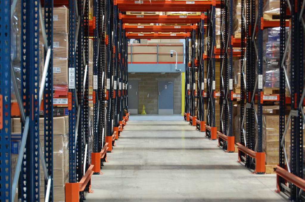 Organized electrical surplus warehouse with pallet racks of breakers, switchgear, transformers, and wire reels
